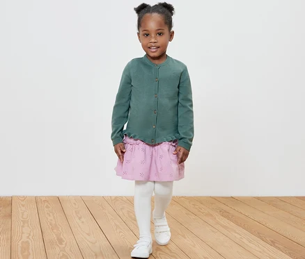 Fillette souriante posant en veste en maille pour enfant.