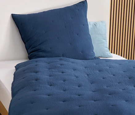 Gros plan d'une parure de lit bleu marine avec motif matelassé et oreiller sur un lit.