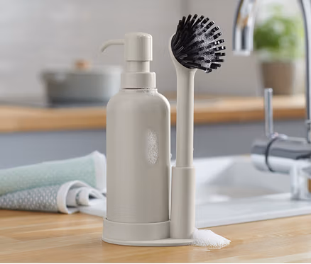 Un lot d’accessoires de vaisselle comprenant un distributeur de savon et une brosse sur un comptoir de cuisine.