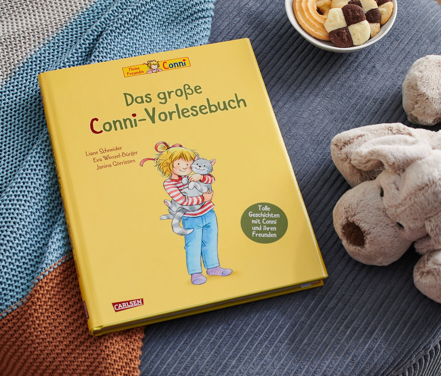 Sur un tabouret bleu sont posés le livre jaune «
Das große Conni-Vorlesebuch
», un chien en peluche, un bol de biscuits et une couverture tricotée.