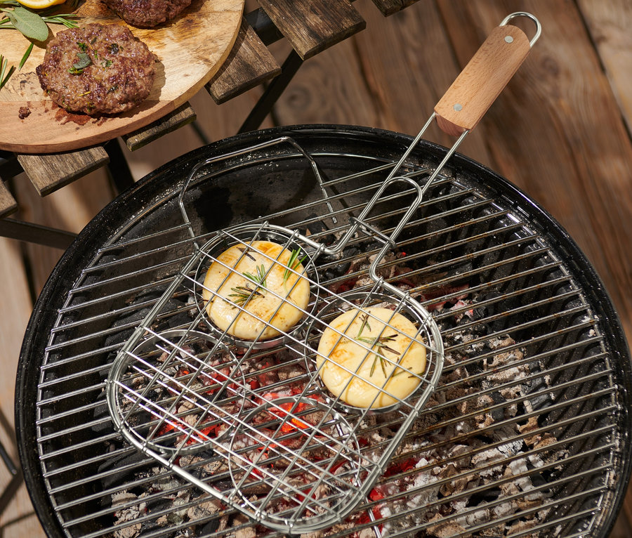 Deux burgers sont en train de cuire dans une spatule à burger pour barbecue sur un grill, d'autres burgers sont posés sur une planche en bois.