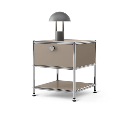 Une lampe grise est posée sur une table d'appoint avec tiroir en métal « CN3 » beige.