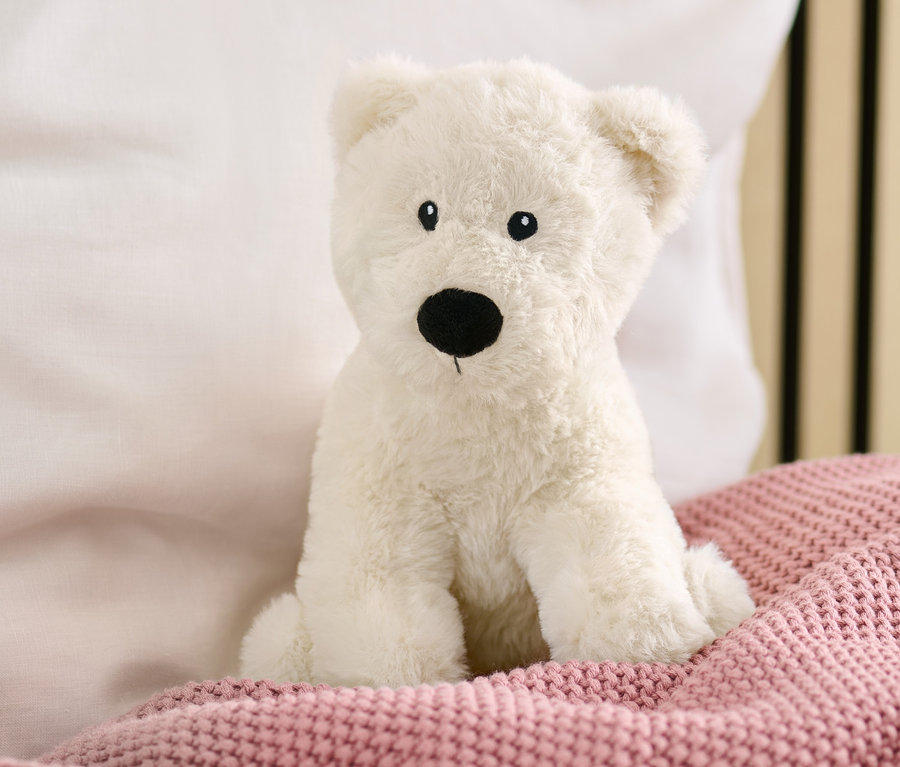 Une peluche ours polaire est assise sur un lit avec une couverture en tricot rose.