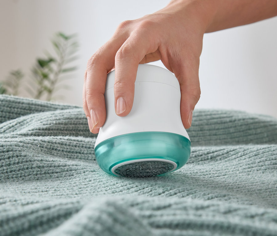 Une main utilise un rasoir anti-bouloches sur un pull.