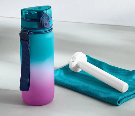 Une gourde isotherme est posée à côté d'une serviette et d'un kettlebell.