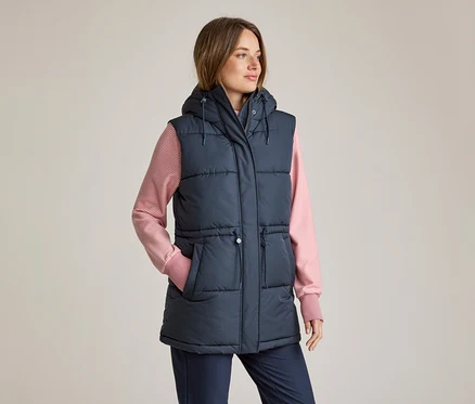 Femme portant un gilet doudoune à capuche bleu marine sur un t-shirt à manches longues rayé rose et blanc et un pantalon bleu marine, la main gauche dans la poche, regardant vers la droite.
