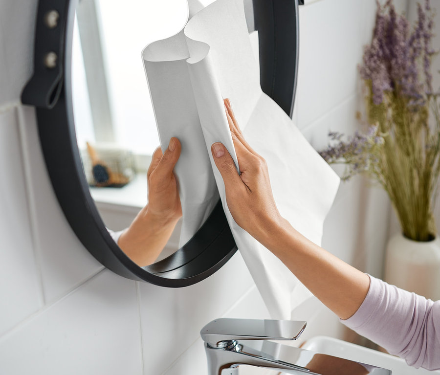 Une femme nettoie un miroir rond avec un chiffon magique dans une salle de bain.