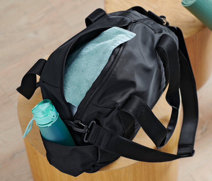 Un sac de sport noir est posé sur un tabouret en bois à côté d'un tapis de yoga enroulé.