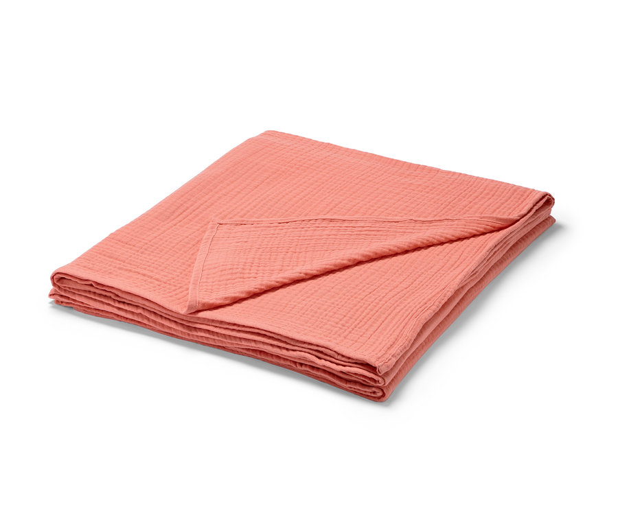 Un couvre-lit en mousseline pêche plié.