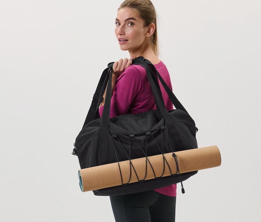 Femme portant un sac de sport noir et un tapis de yoga sur l'épaule.