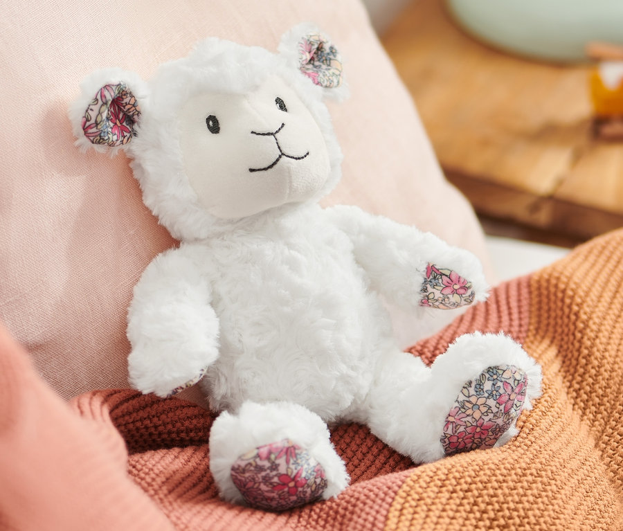Un mouton en peluche est allongé sur un lit avec des oreillers roses et une couverture orange.