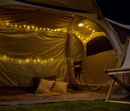 Vue de l'intérieur d'une tente avec des guirlandes lumineuses, des coussins et une couverture.