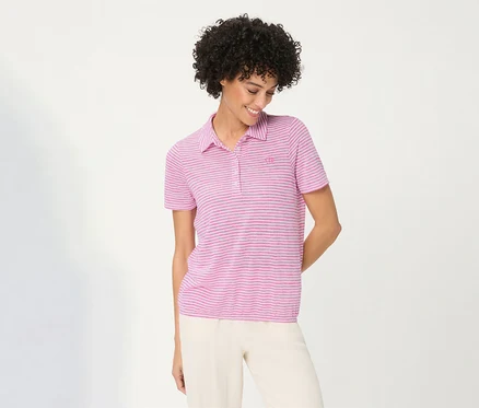 Femme souriante aux cheveux bouclés portant un Polo Olsen rose rayé et un pantalon clair, regardant vers le bas.
