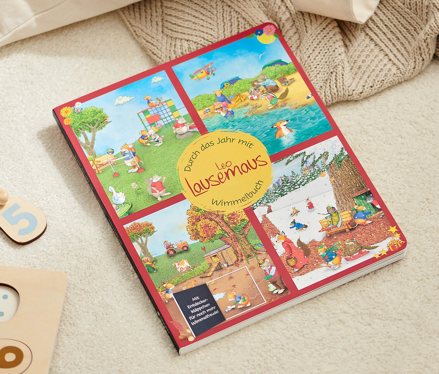 Un livre d’images ouvert «
Durch das Jahr mit Leo Lausemaus » est posé sur un tapis beige à côté d’un puzzle en bois.
