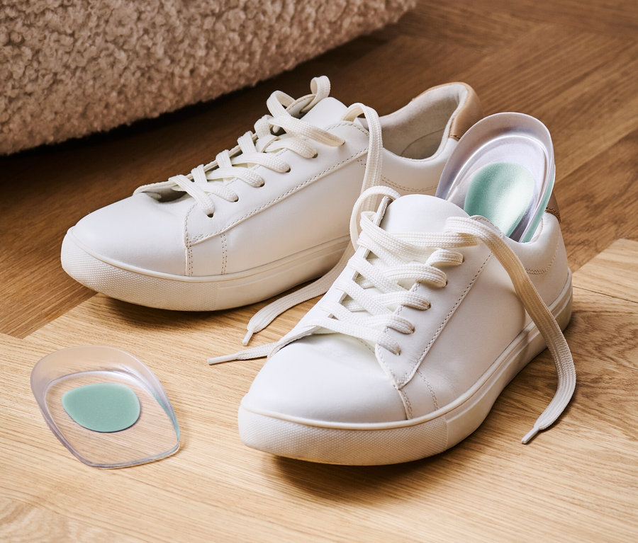 Deux baskets blanches et 1 paire de talonnettes sur un plancher en bois.