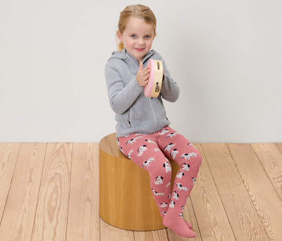 Une fille assise joue du tambourin et porte des collants thermiques roses et gris pour enfants.
