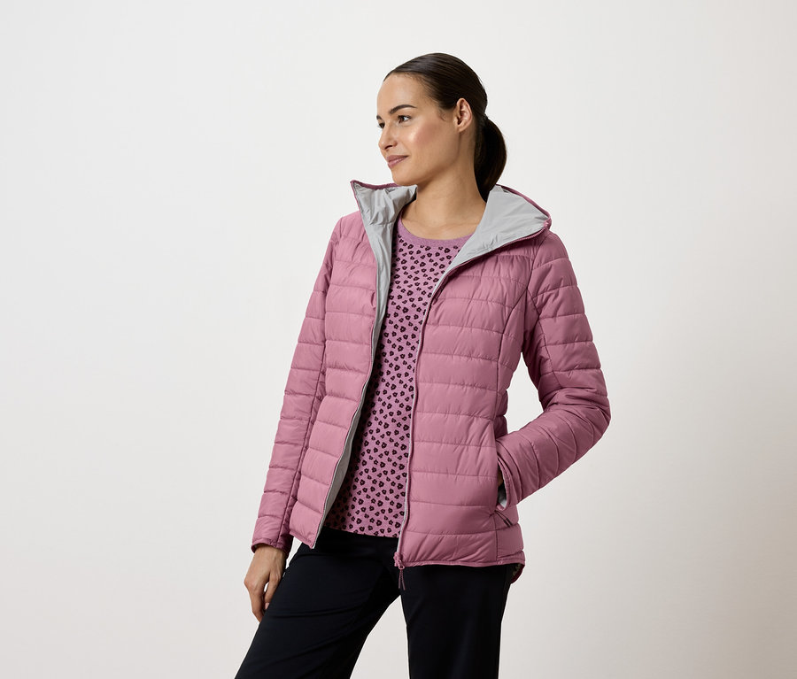 Femme portant une veste matelassée rose avec capuche et un pantalon bleu marine, regardant vers la gauche.