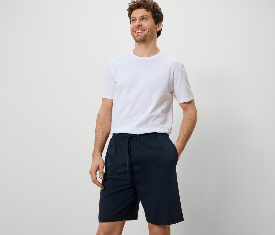 Un homme portant un t-shirt blanc et 2 shorts de pyjama bleu marine sur fond blanc.