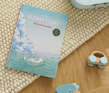 Le livre « Kleiner Eisbär – bärenstarke Geschichten » posé sur un tapis beige à côté de jouets en bois.