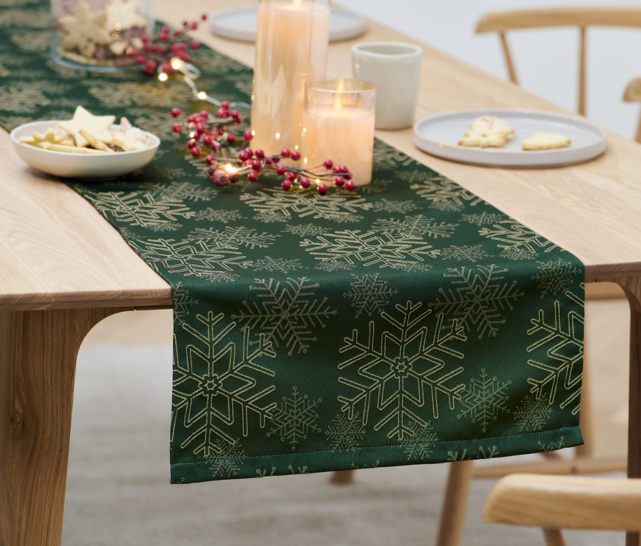 Sur une table, un chemin de table en jacquard vert avec des décorations de Noël.