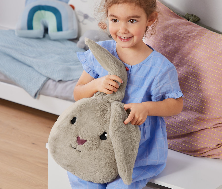Une fille en pyjama bleu tient un coussin en peluche petit lapin.