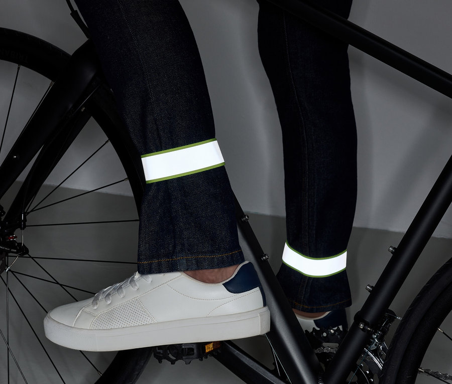 Jambes sur un vélo en jean avec des bandes réfléchissantes et des chaussures blanches.