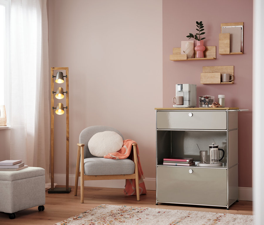 Salon avec fauteuil, lampe et commode avec machine à café. Sur la commode, un panier à capsules, blanc.