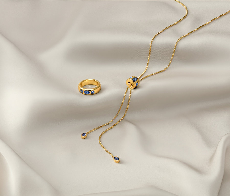 Sur un tissu blanc reposent une chaîne dorée «Iconic» et une bague dorée «Iconic».