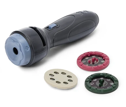 Un jouet gris foncé en forme de lampe de poche avec une extrémité bleu clair et un bouton bleu clair. À côté se trouvent trois disques ronds : un beige, un rouge et un vert foncé, tous avec des motifs pour la projection.
