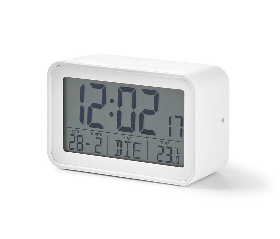 Un réveil LCD numérique blanc affiche l'heure 12:02, la date 28-2 et une température de 23 degrés Celsius.
