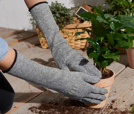 Une femme rempote une plante dans un pot en portant des gants de protection anti-coupures gris.
