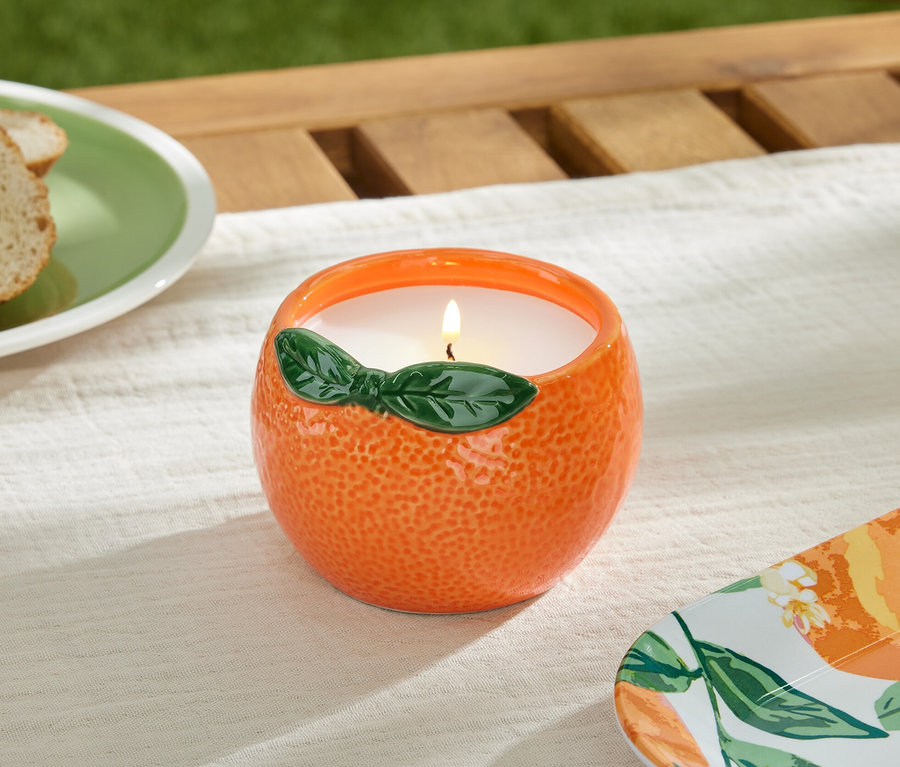 Une bougie à la citronnelle allumée dans un récipient orange sur une table.