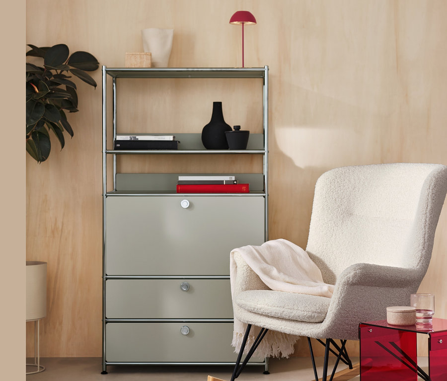 Une étagère grise se trouve à côté d'une chaise à bascule en tissu bouclette et d'une lampe de table à LED sans fil rouge ainsi que d'une table d’appoint en verre acrylique.