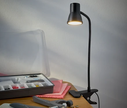 Une lampe LED noire à pince est posée sur une table à côté d'une trousse de couture.