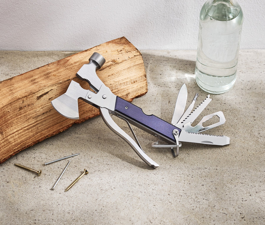 Sur une table sont posés un outil multifonction, un morceau de bois, des clous, des vis et une bouteille d'eau.
