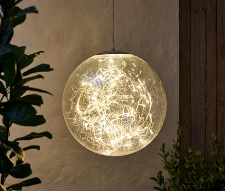 Une boule LED suspendue d'environ 40 cm, éclairée, à côté de plantes.