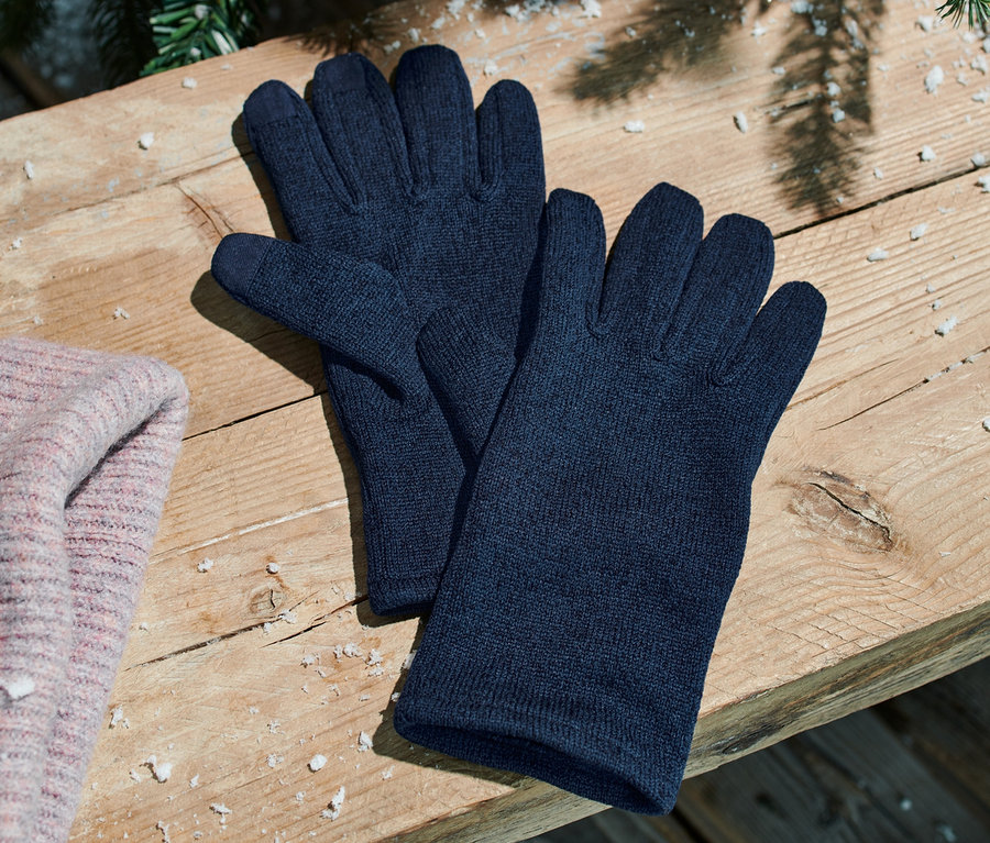 Des gants bleus en polaire tricotée sont posés sur un banc en bois à côté d'un bonnet rose.