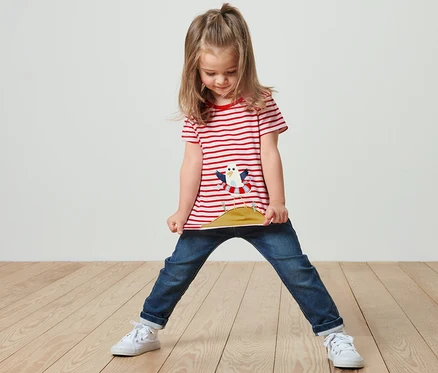 Une fille se tient debout et tient l'ourlet de son t-shirt rayé rouge avec application.