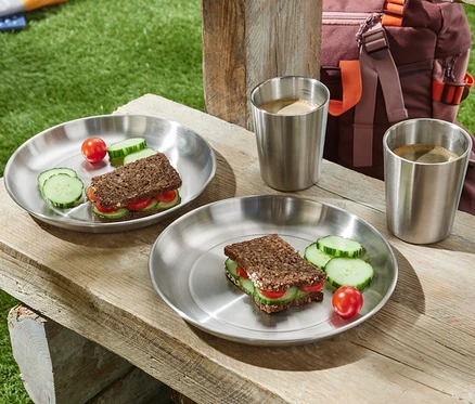 Deux assiettes de camping avec sandwichs, concombre et tomate sur une table en bois.