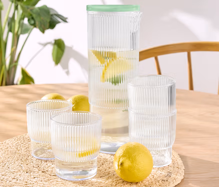 Sur une table, quatre gobelets en plastique avec pichet, certains remplis d'eau et de citron.