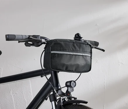 Vue détaillée d'un vélo noir avec une sacoche de guidon noire et un phare de vélo devant un mur blanc.