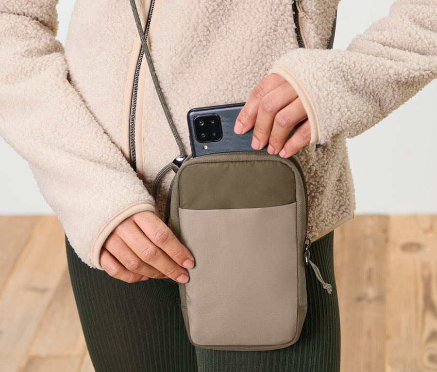 Une femme met un téléphone portable dans une pochette antigel taupe pour téléphone portable.