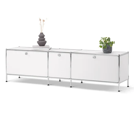 Meuble bas « CN3 » blanc avec 3 abattants. Un vase, un livre et une plante en pot sont posés sur le meuble.
