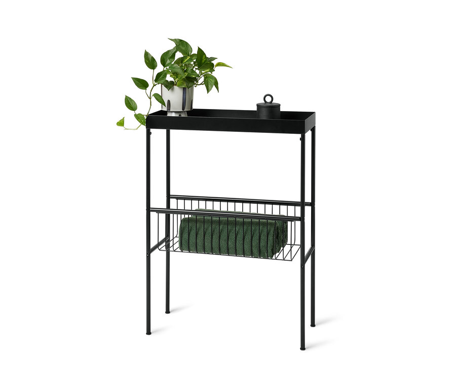 Console étroite noire avec étagères, avec une plante et une boîte noire avec couvercle sur l'étagère supérieure et une serviette verte sur l'étagère inférieure.