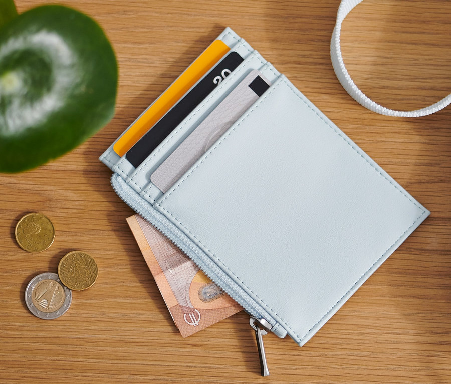Sur une table en bois sont posés un porte-monnaie bleu clair, des pièces de monnaie et un sac.