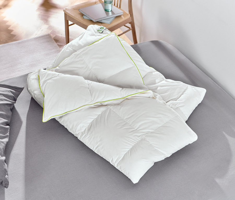 Une couette mi-saison en duvet irisette® blanche est posée sur un lit.