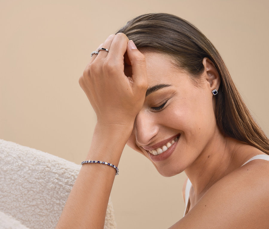 Femme souriante portant une bague, un bracelet et des boucles d'oreilles.