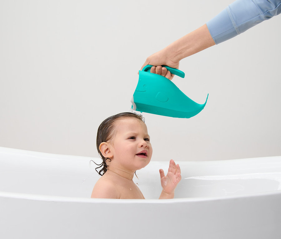 Un parent lave les cheveux d'un enfant avec un Gobelet lave-cheveux pour enfant dans une baignoire.