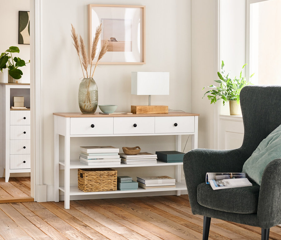 Intérieur d'un salon avec un fauteuil rembourré anthracite, une console à tiroirs et une lampe de table avec pied en bois.