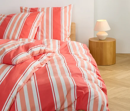 Vue détaillée de la parure de lit corail rayée renforcée de taille standard et grande taille sur un lit.